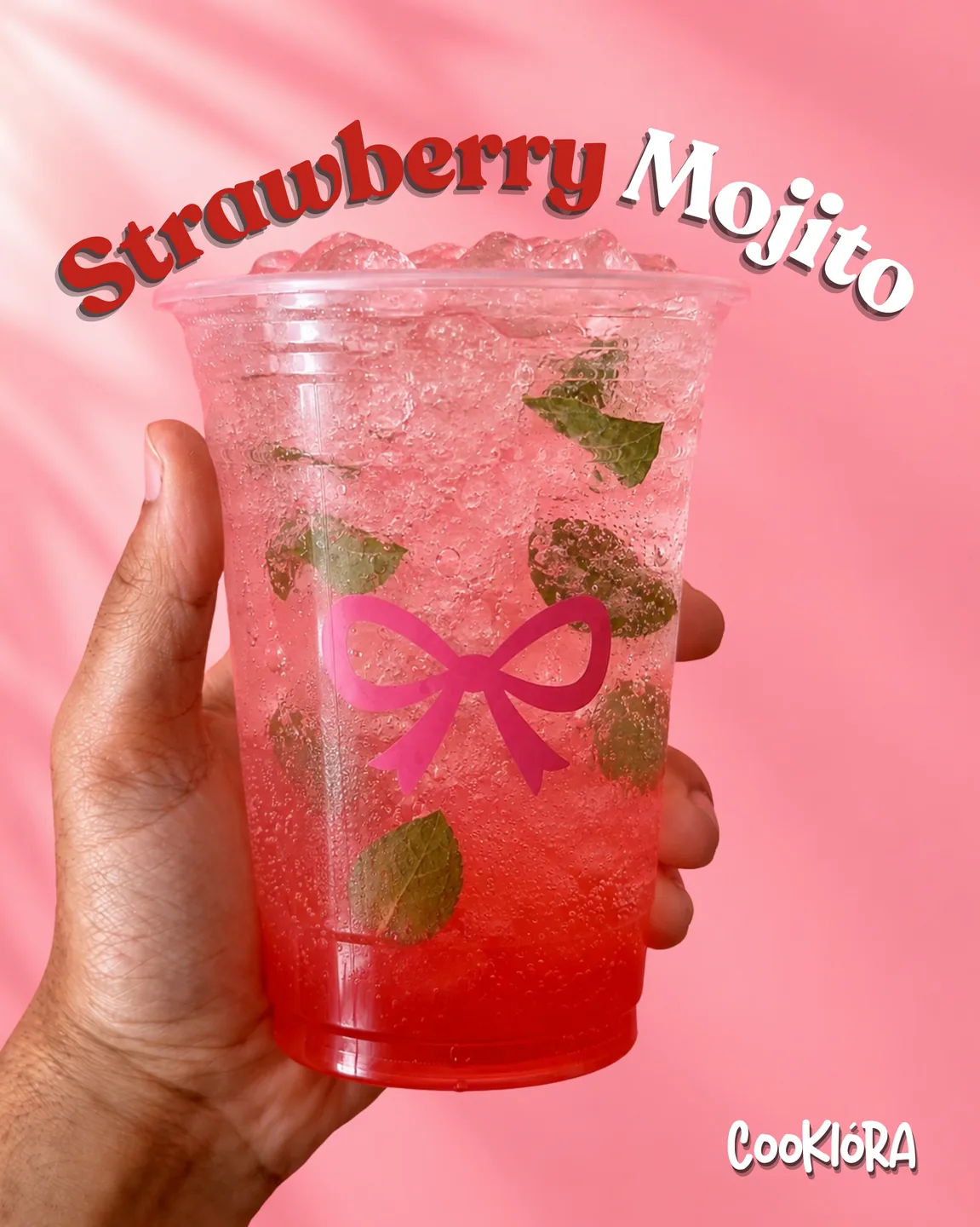 A hand holding a Strawberry Mojito with a pink bow on the cup