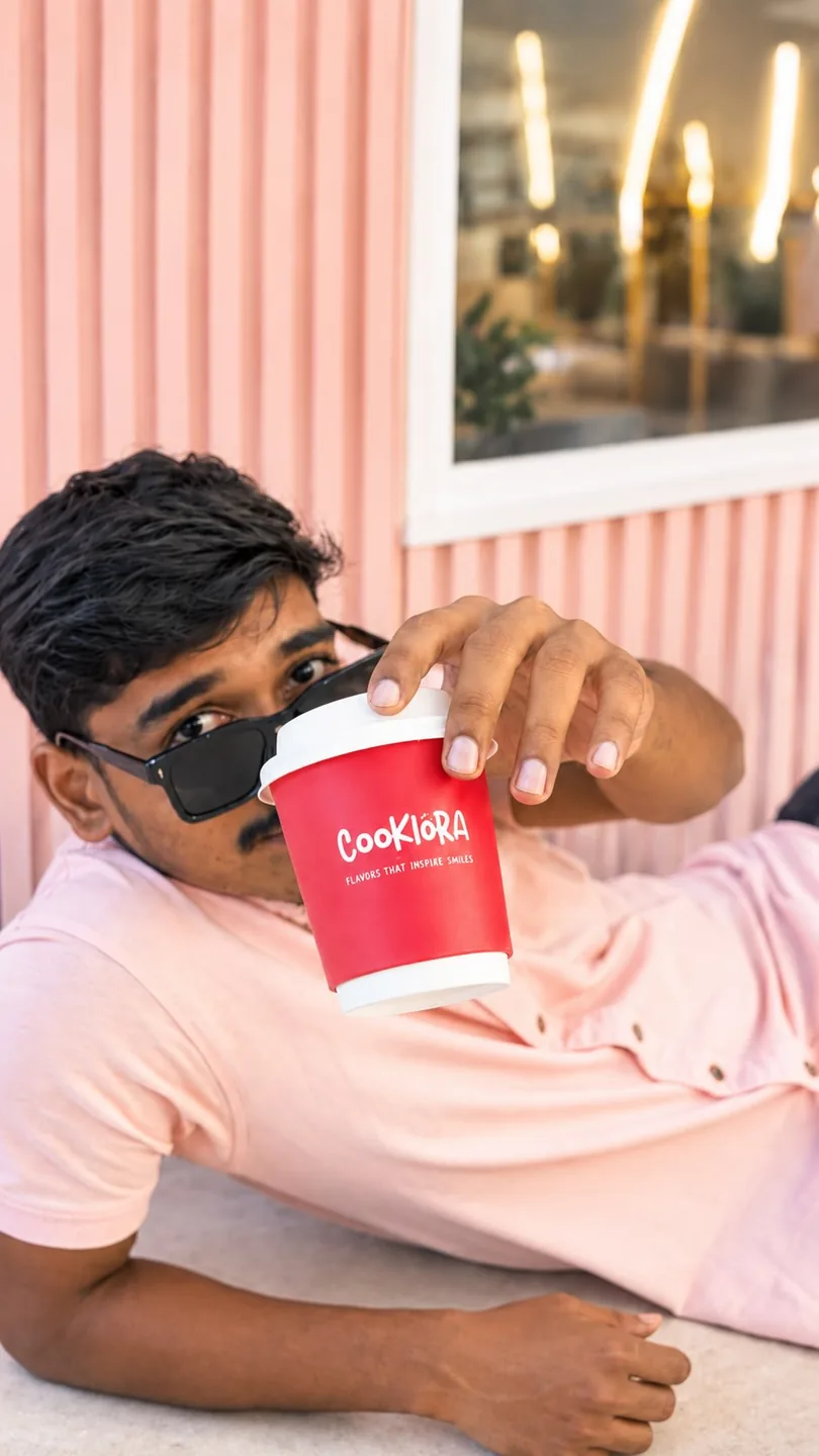 A man lying back, holding a Cookiora coffee cup to the camera