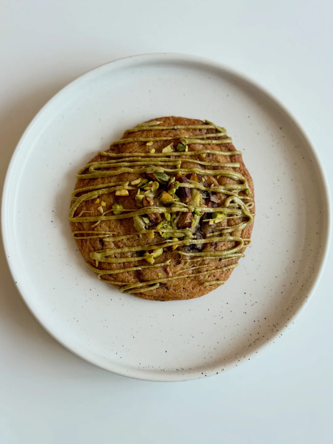 A pistachio cookie drizzled with pistachio cream on a white plate